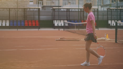 A-woman-walks-on-a-tennis-court-with-a-racket-and-knocks-the-ball-on-the-ground.-concentration-will-to-win